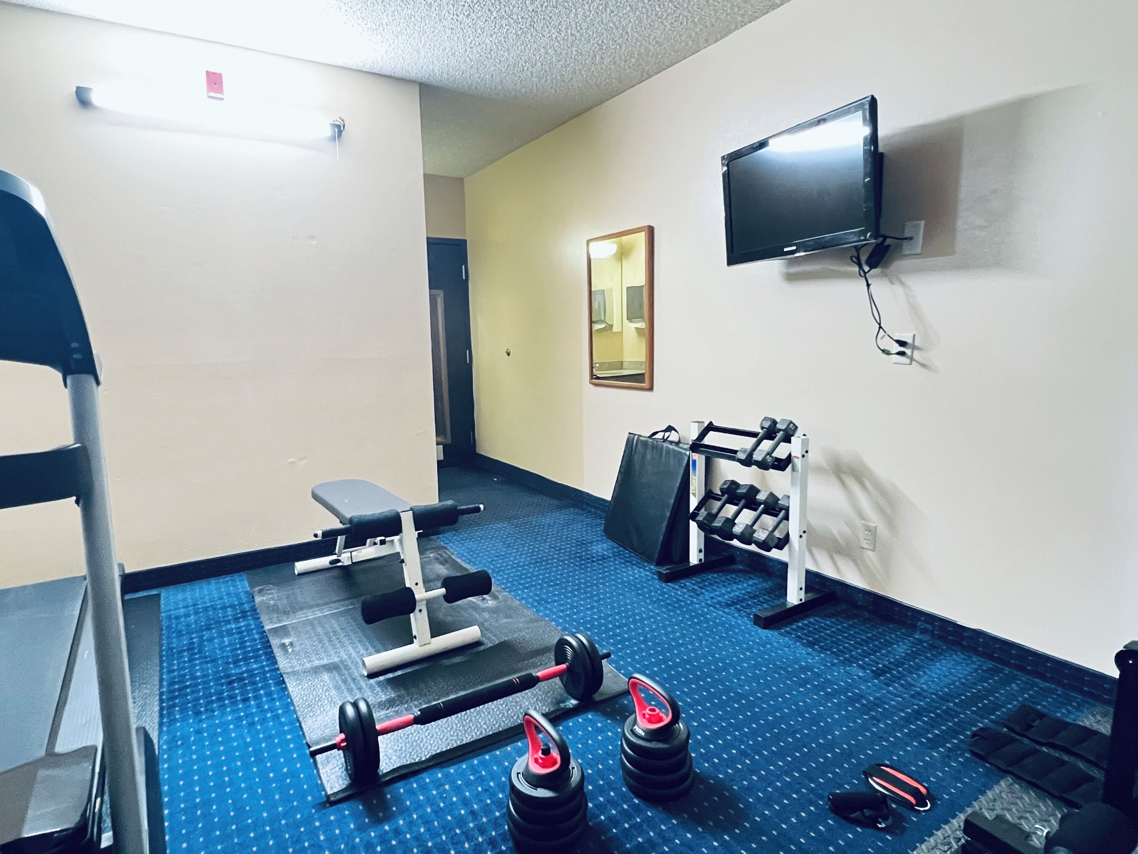 A gym with exercise equipment, a bench, a mirror, and a TV on the wall.