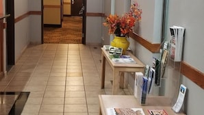 A hotel hallway with a reception desk, a vase of flowers, and a bulletin board with pamphlets. - Hometown Inn & Suites (Washington)
