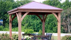 A wooden gazebo with a roof, surrounded by a bench and a planter with flowers. - Hometown Inn & Suites (Washington)