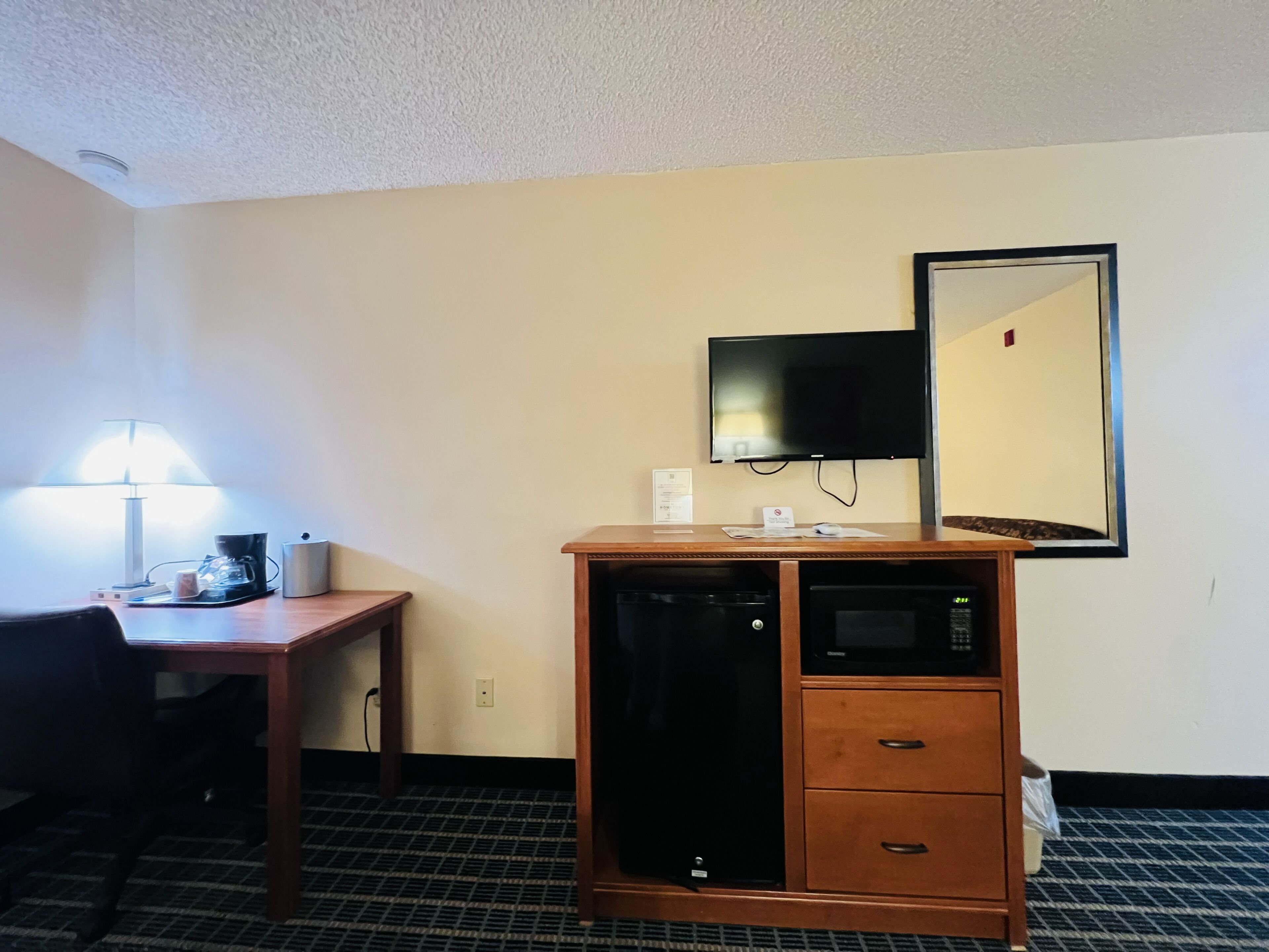 Hotelkamer met bureau, stoel, koffiezetapparaat, magnetron en een flatscreen televisie aan de muur.