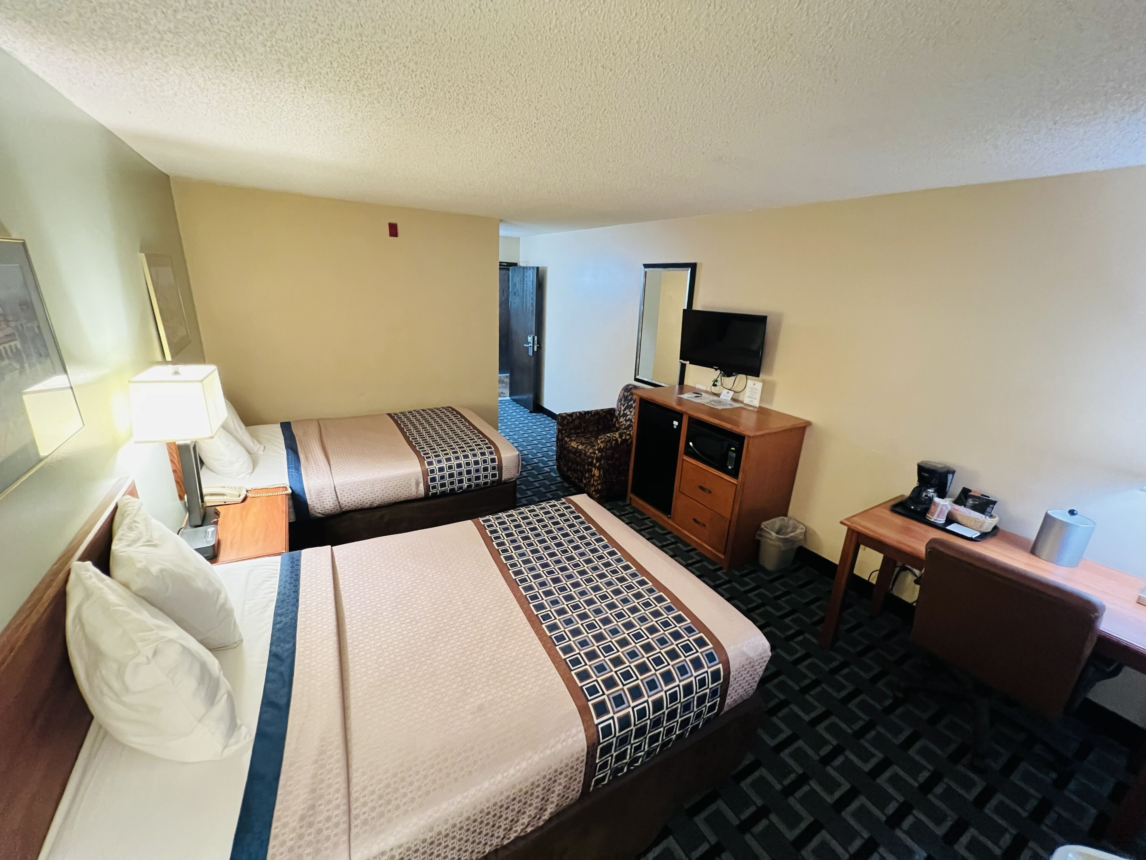 A hotel room with two beds, a desk, a TV, and a coffee maker.