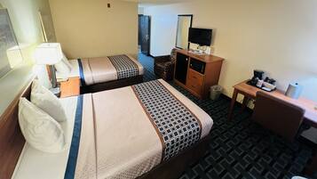 A hotel room with two beds, a desk, a TV, and a coffee maker.