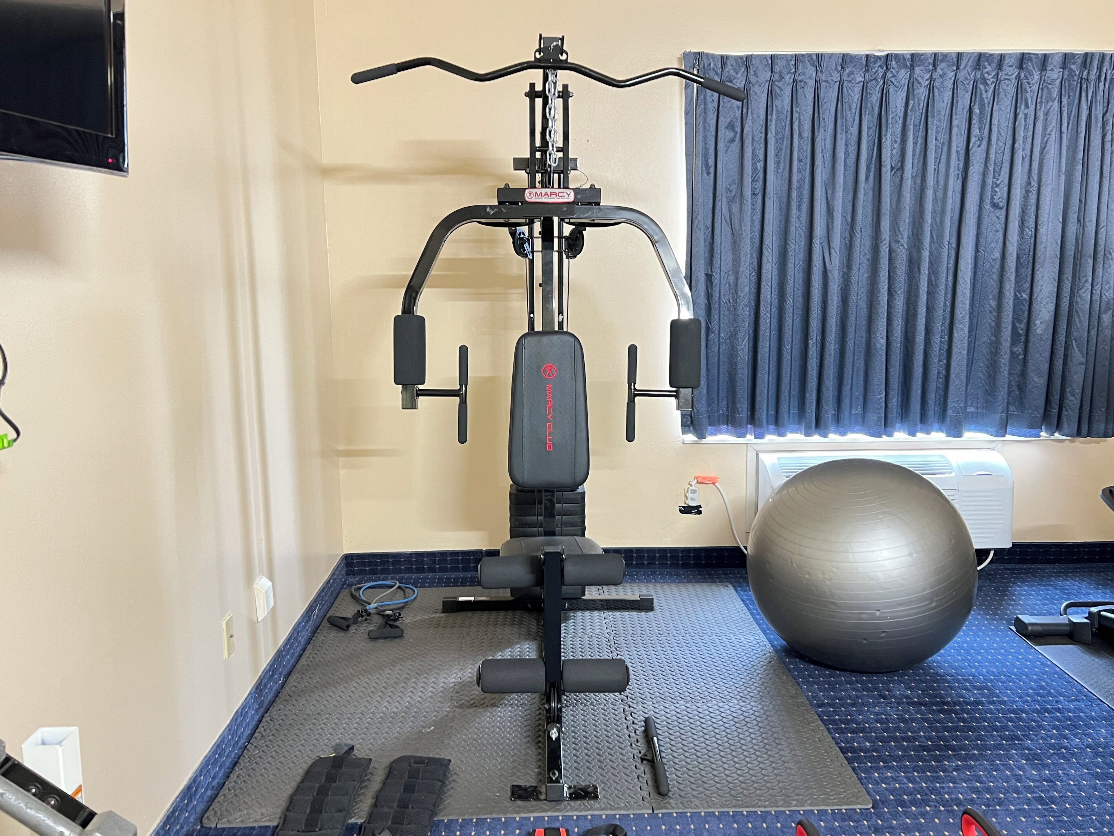 Un gimnasio en casa con una bicicleta estática, una pelota de ejercicios y una colchoneta.