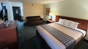 A hotel room with a bed, a desk, a sofa, a lamp, and a television. - Hometown Inn & Suites (Washington)