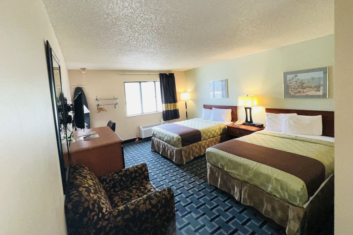 A hotel room with two beds, a desk, a chair, a TV, and a window with curtains.