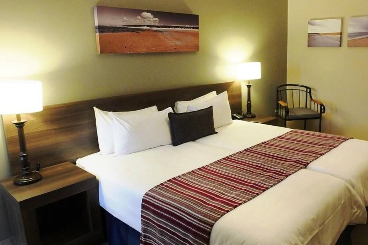 A double bed with white and red striped bedding, two bedside tables with lamps, a wooden headboard, and a chair.