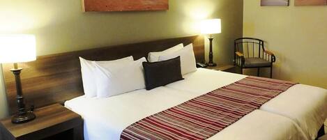 A double bed with white and red striped bedding, two bedside tables with lamps, a wooden headboard, and a chair.