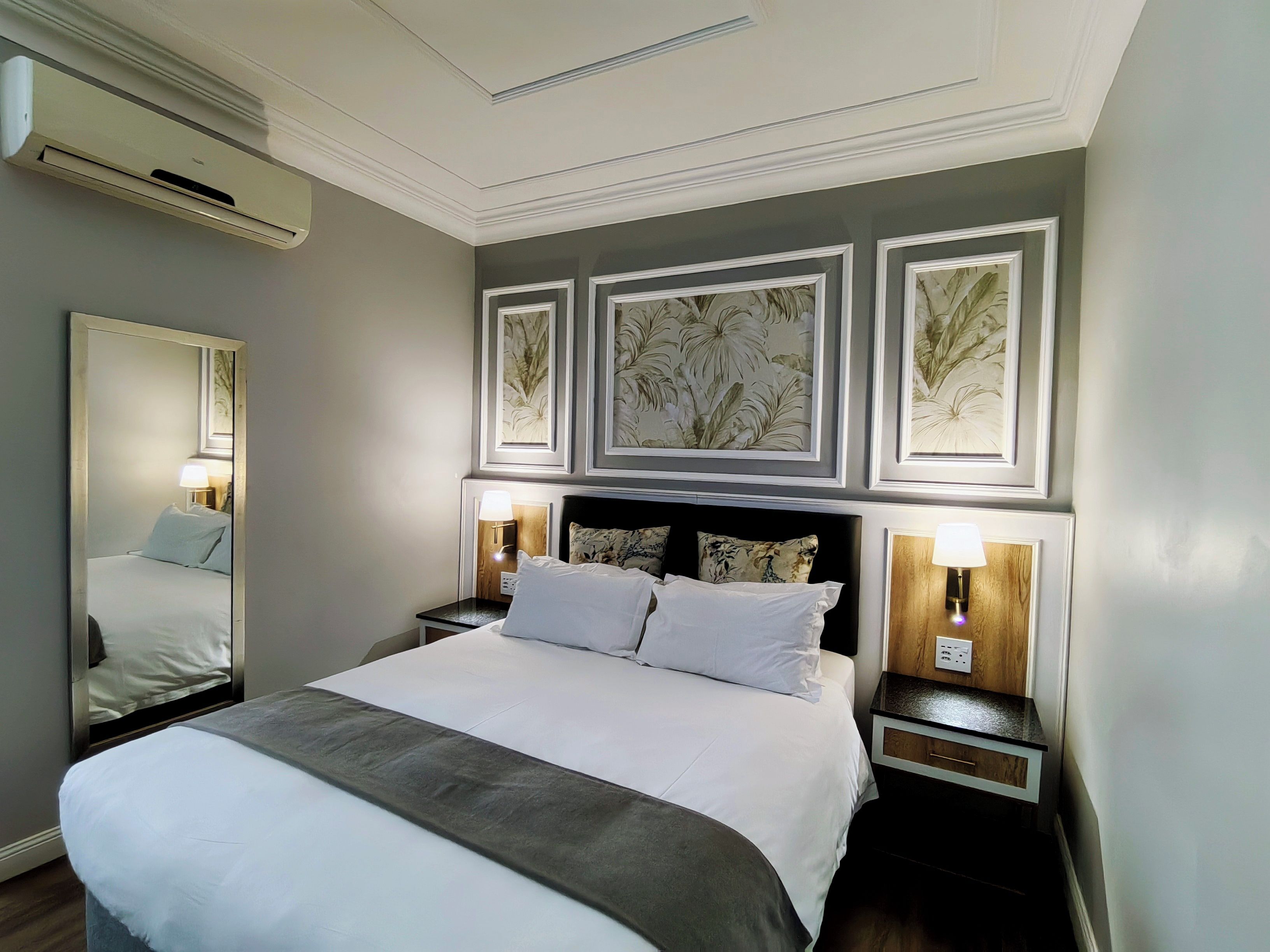 Ein Hotelzimmer mit einem großen Bett, zwei Nachttischen mit Lampen, einem Spiegel und drei gerahmten floralen Wandbildern.