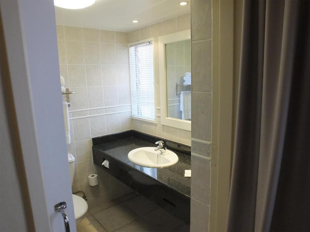 A modern bathroom with a white sink, dark countertop, and beige tiles.