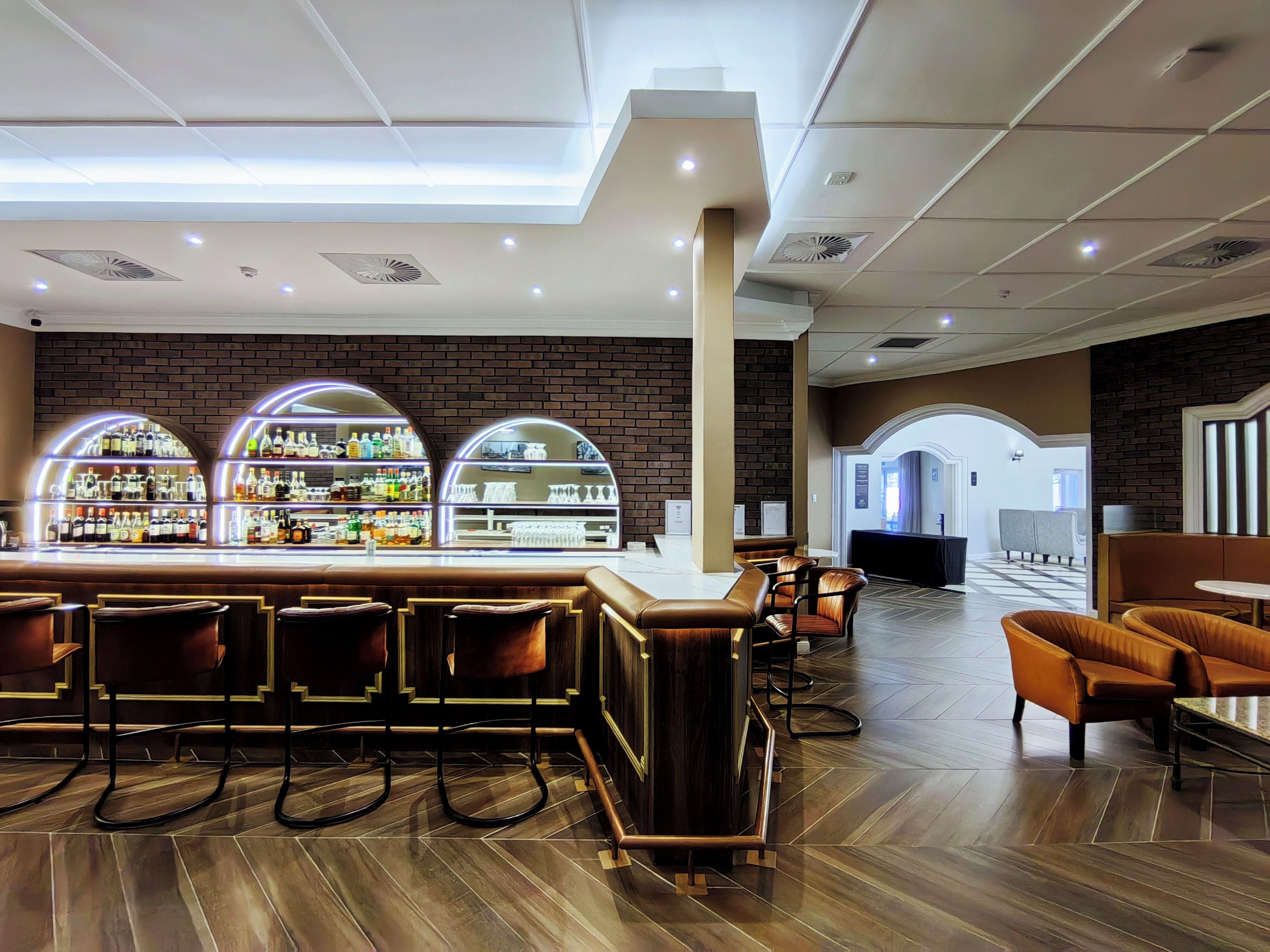 A bar area with a brick wall, bar stools, and a counter displaying bottles.