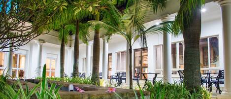 A covered outdoor area with palm trees, stone benches, and a fountain.