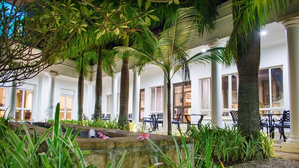 A covered outdoor area with palm trees, stone benches, and a fountain. - Premier Hotel The Richards (Richards Bay)