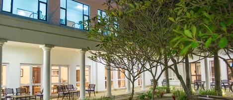 A building with a covered outdoor area featuring a seating arrangement and a tree.