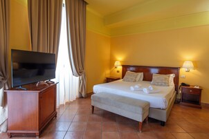 Habitación de hotel con cama, lámparas de noche, un televisor sobre un mueble de madera y un banco.