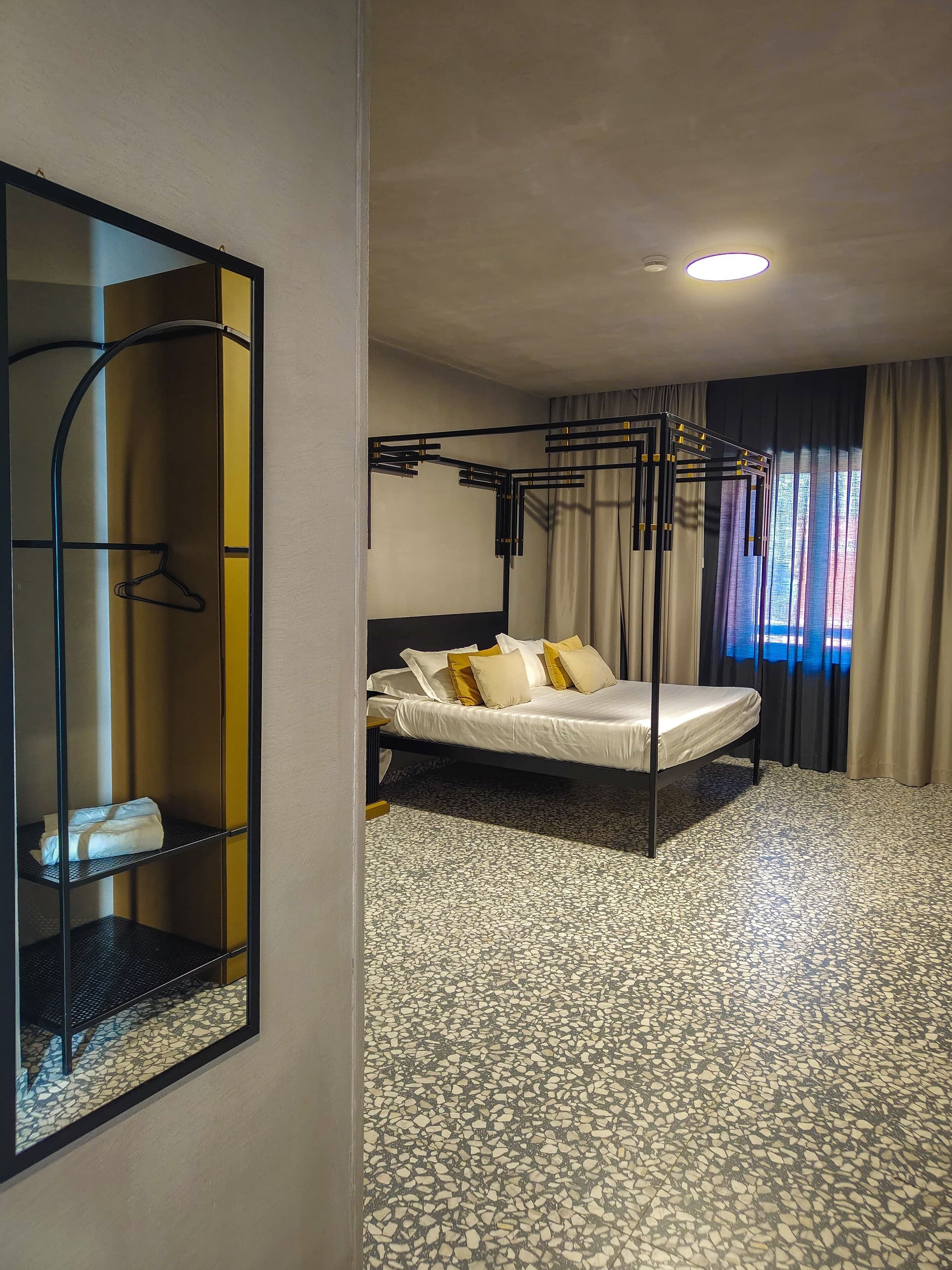 A hotel room with a bed, a mirror, a wardrobe, and a ceiling light.