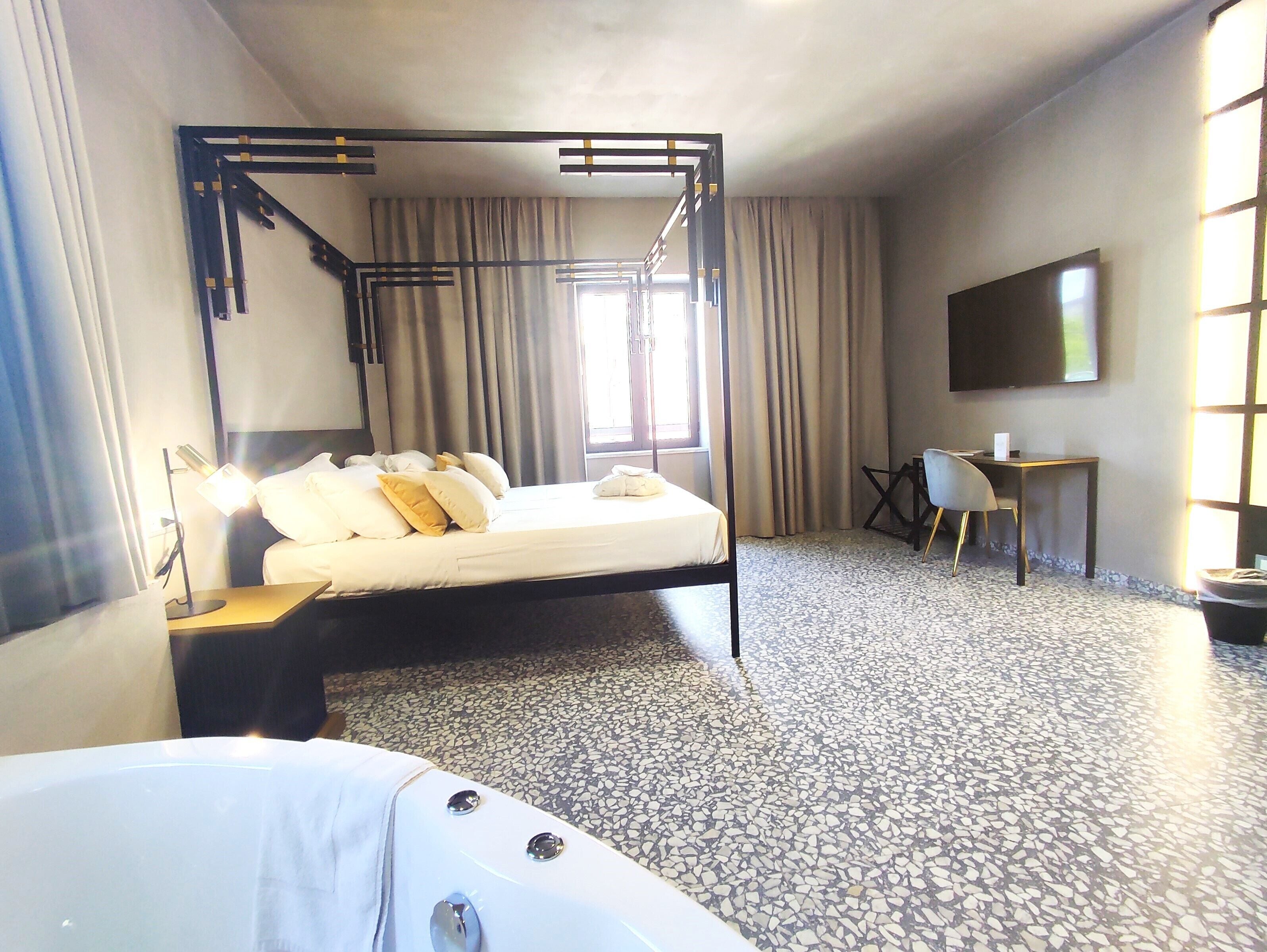 Habitación de hotel con cama con dosel, un escritorio, una silla y un televisor en la pared.