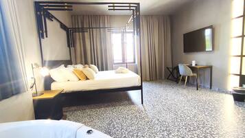Habitación de hotel con cama con dosel, un escritorio, una silla y un televisor en la pared.