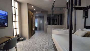 Habitación de hotel con cama, escritorio, silla, un espejo grande y televisor en la pared.