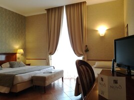 Una camera d'albergo con un letto, una scrivania con un computer, una lampada e una finestra con tende.