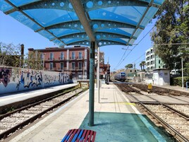 Un andén de estación de tren con marquesina azul, grafitis en la pared y vías.