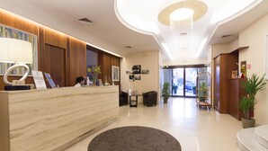 Uma área de recepção moderna com balcão de mármore, um tapete grande e escuro, e vista para o saguão.
