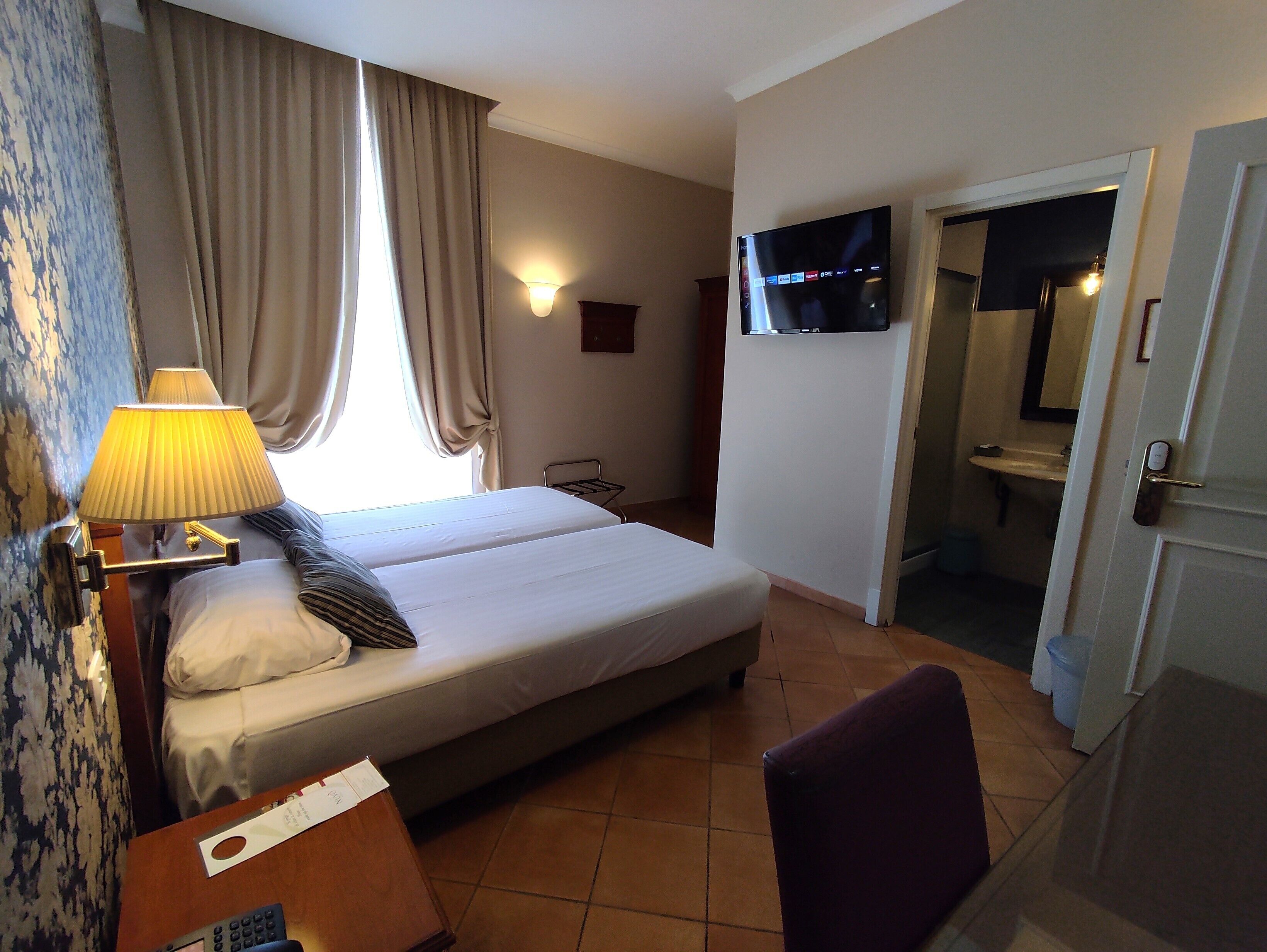 Een hotelkamer met een bed, een bureau met een lamp, een televisie en een badkamer die door een open deur zichtbaar is.