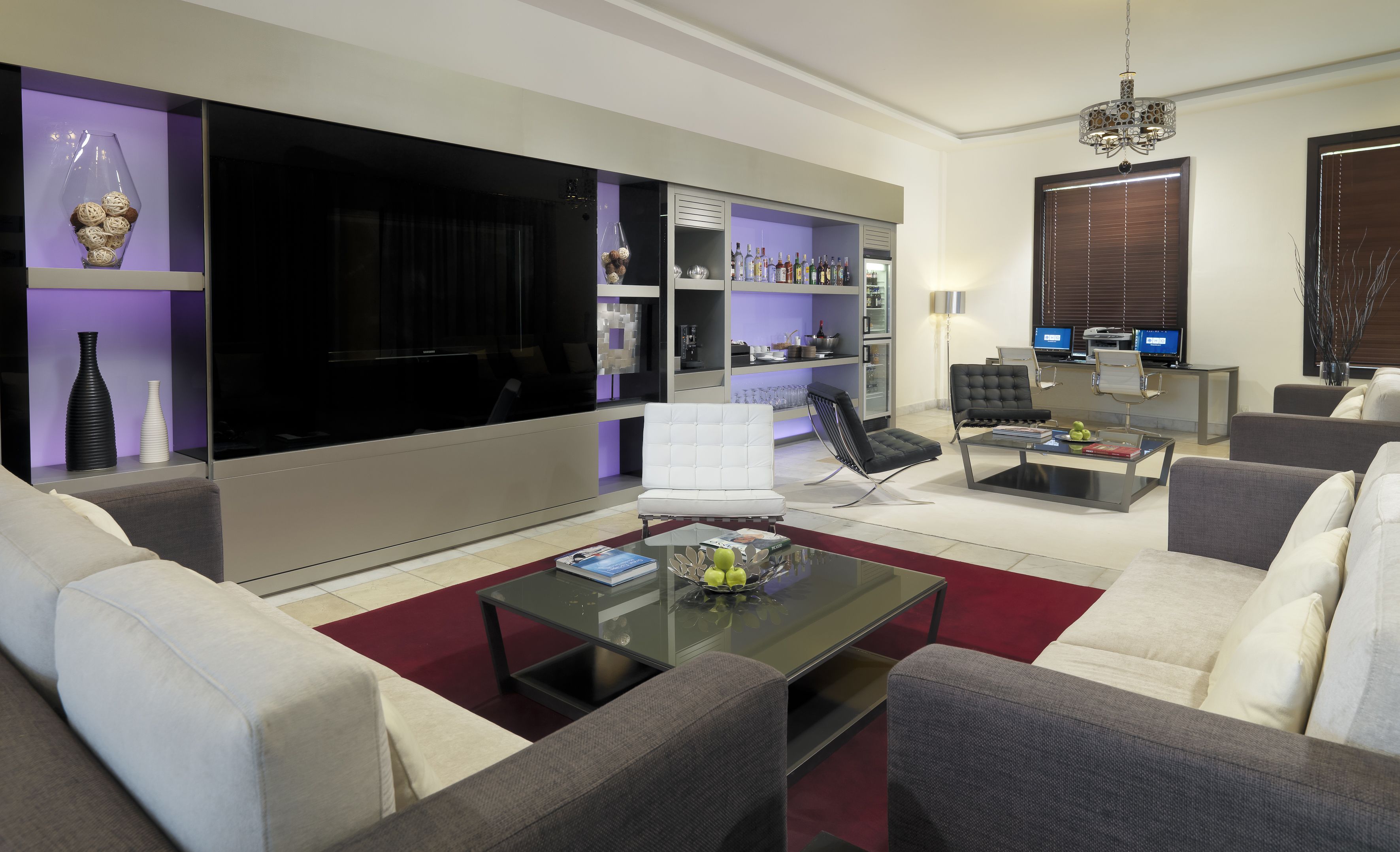 Una sala de estar moderna con un televisor de pantalla plana grande, asientos cómodos, una mesa de centro y una estantería con diversos objetos.