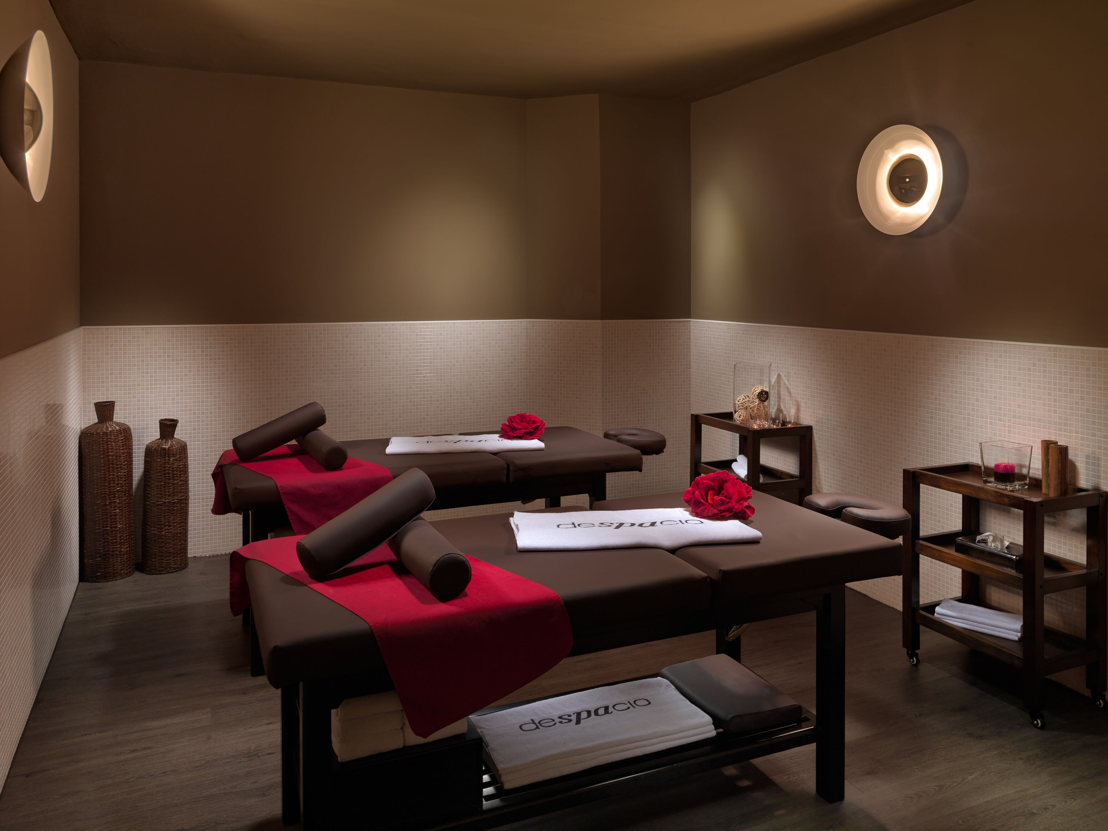 Un cuarto de spa con dos camillas de masaje, toallas rojas y un estante con adornos.