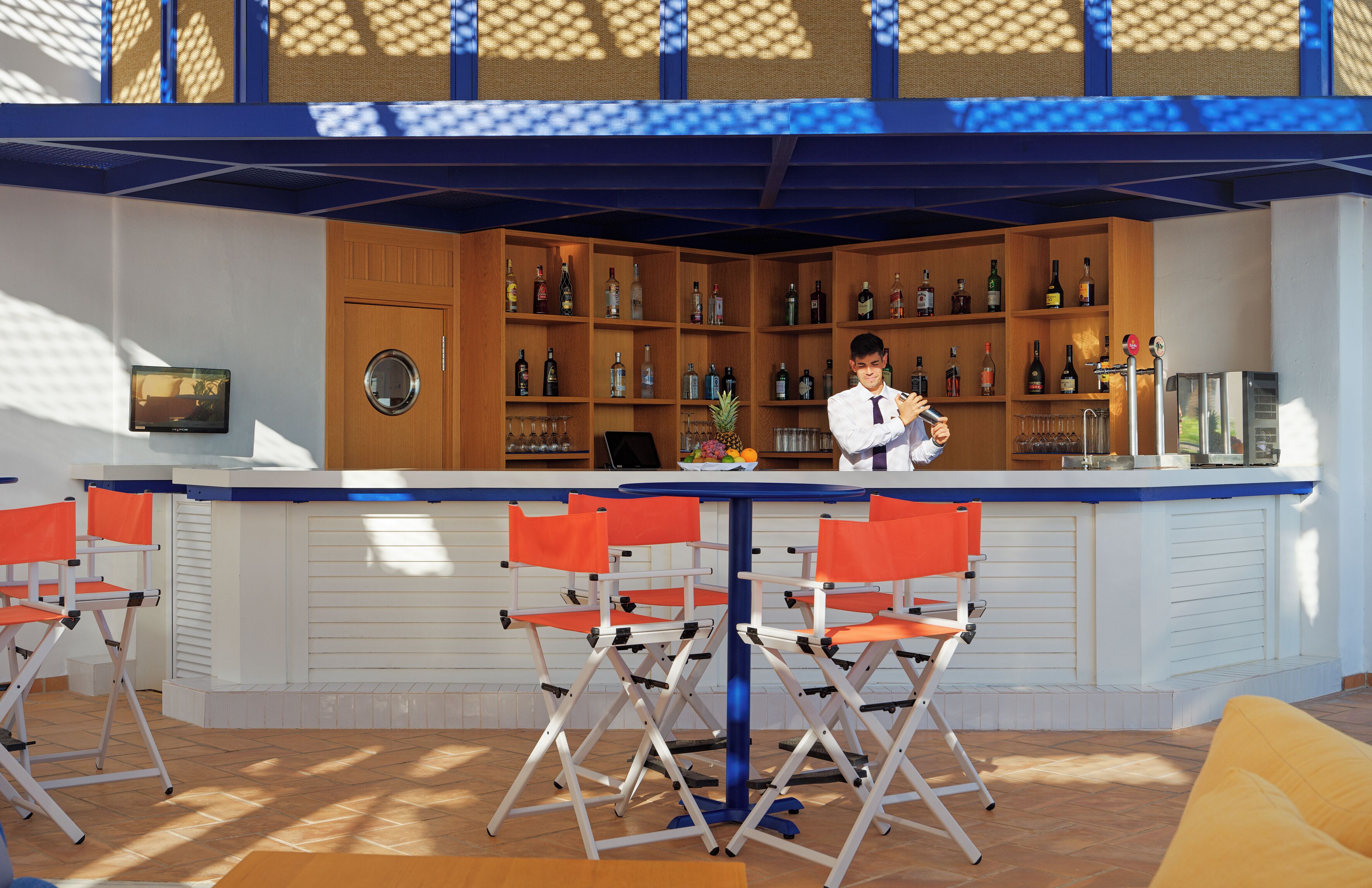 Un espace bar avec un comptoir, de nombreuses étagères remplies de bouteilles et des chaises orange.