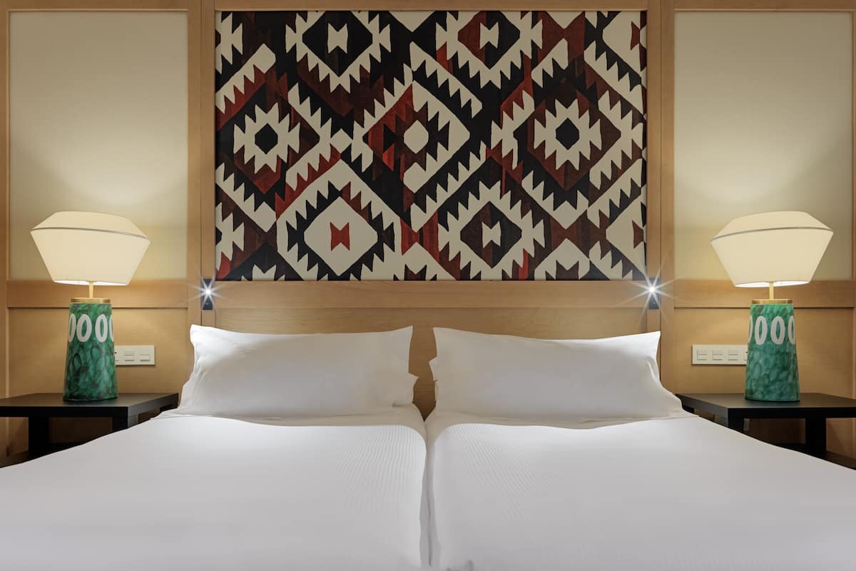 A hotel room with a large bed, two bedside lamps, and a patterned wall hanging.