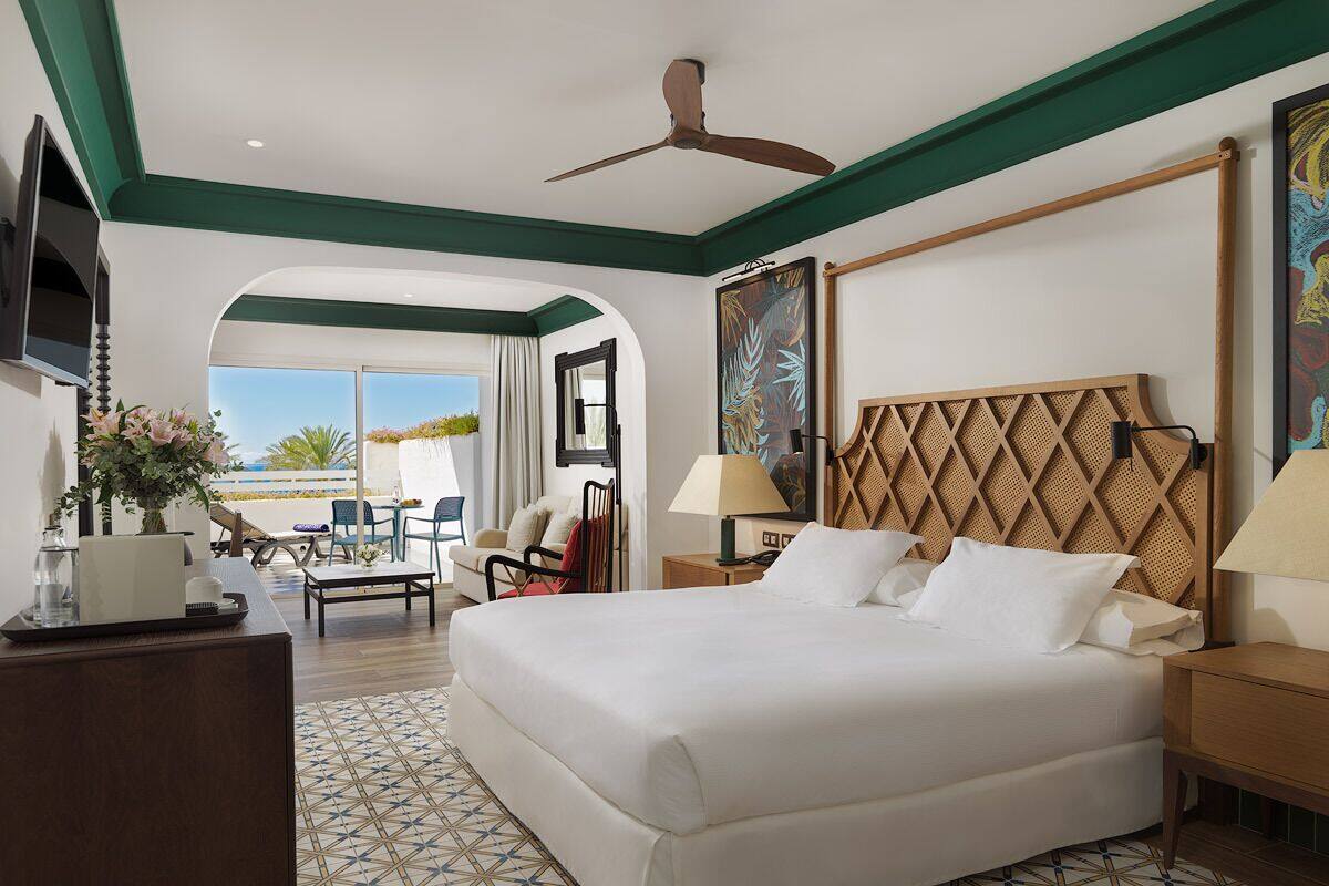 A spacious hotel room with a large bed, a ceiling fan, a TV, and a view of the outdoors.