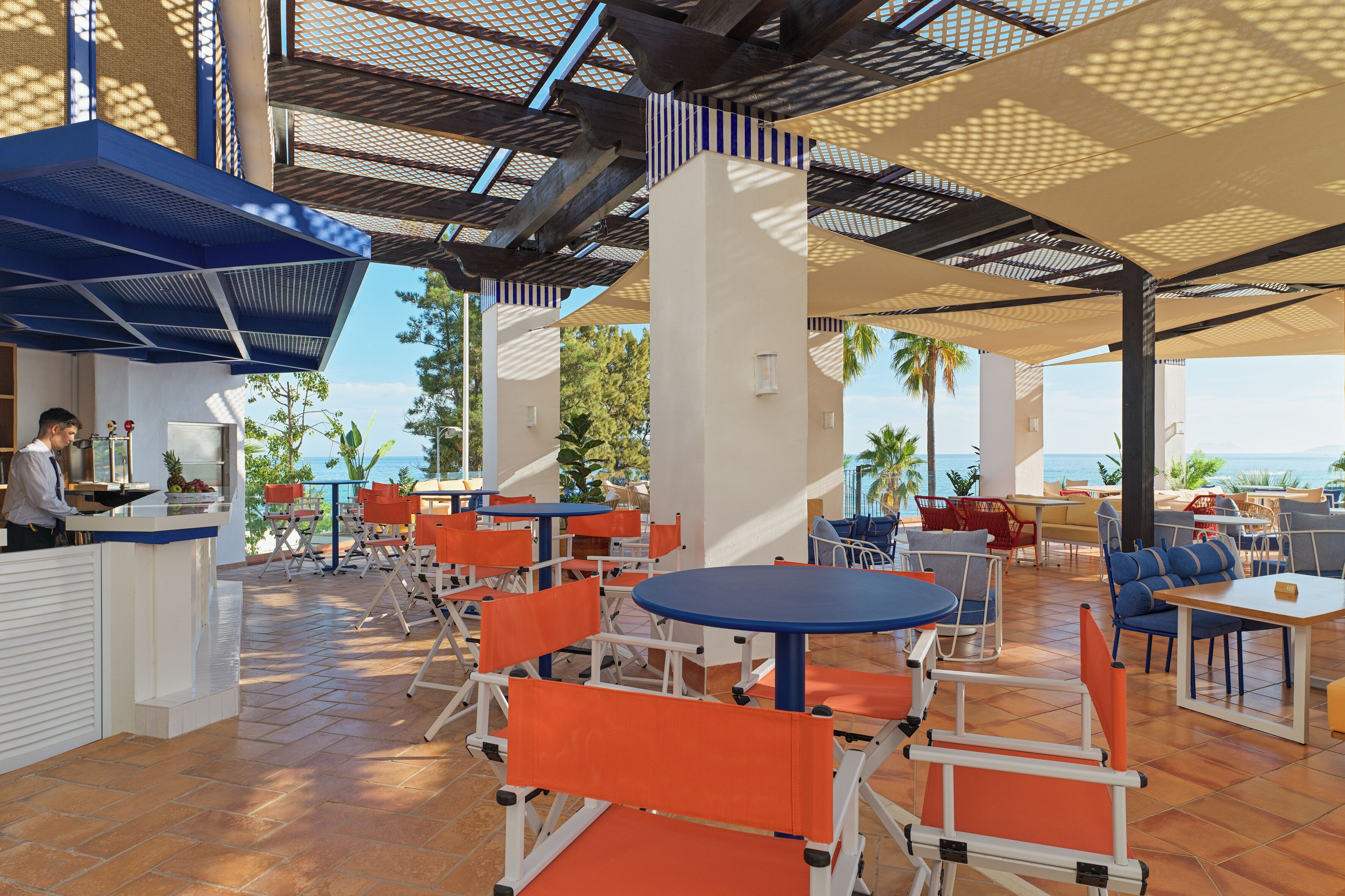 An outdoor seating area with tables and chairs, a counter, and a view of the ocean.