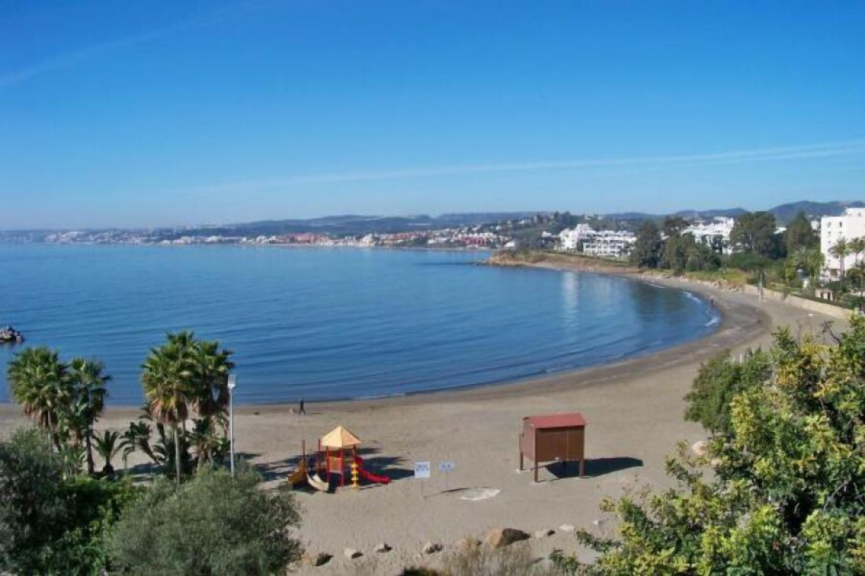 A beach with a small play area, a lifeguard tower, and a clear view of the sea and distant buildings.