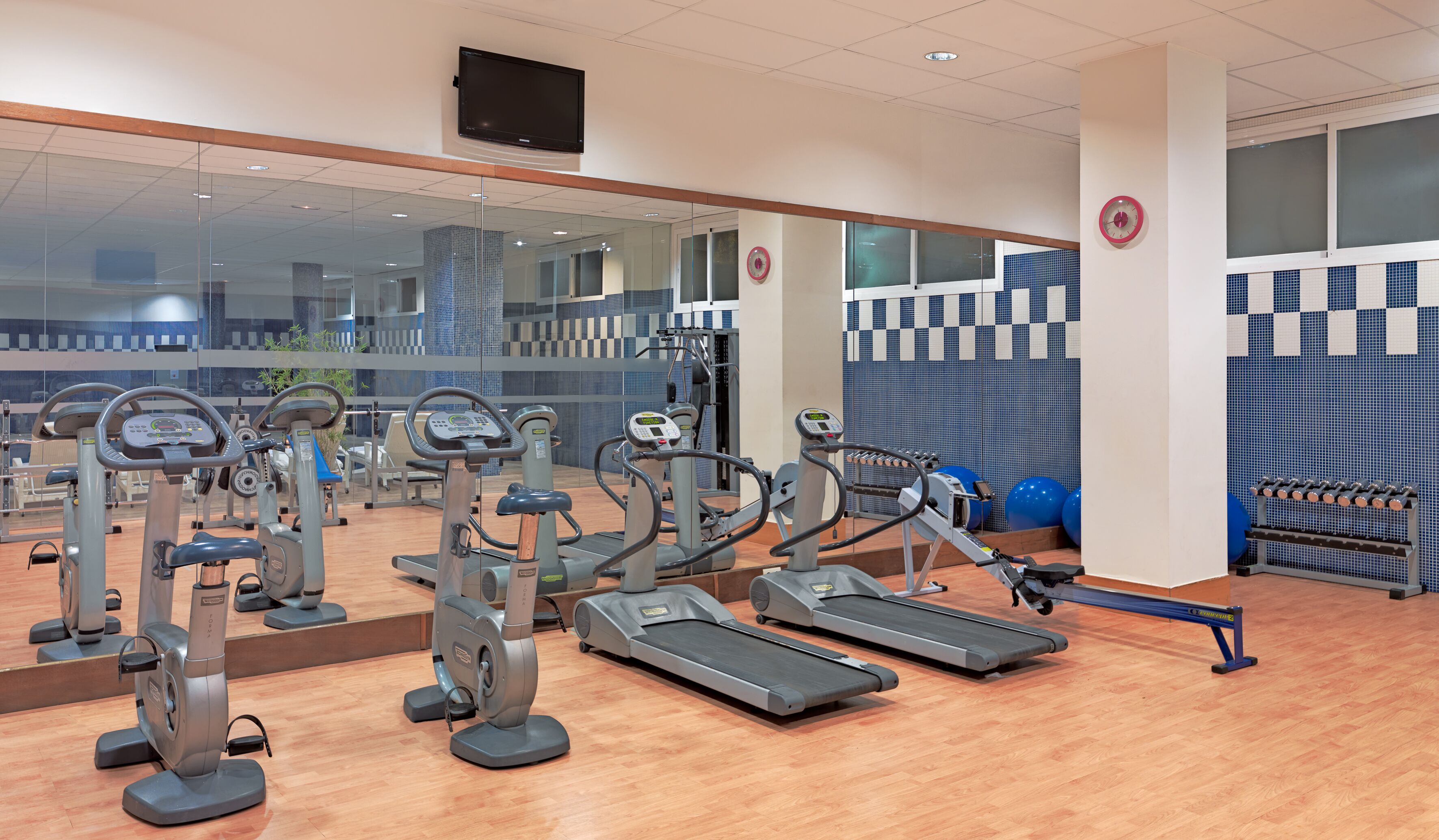 Une salle de sport équipée de divers appareils d’exercice, notamment des tapis de course et des appareils elliptiques, et dotée d’un grand miroir qui reflète l’espace.