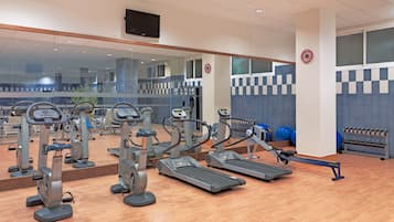 Une salle de sport équipée de divers appareils d’exercice, notamment des tapis de course et des appareils elliptiques, et dotée d’un grand miroir qui reflète l’espace.
