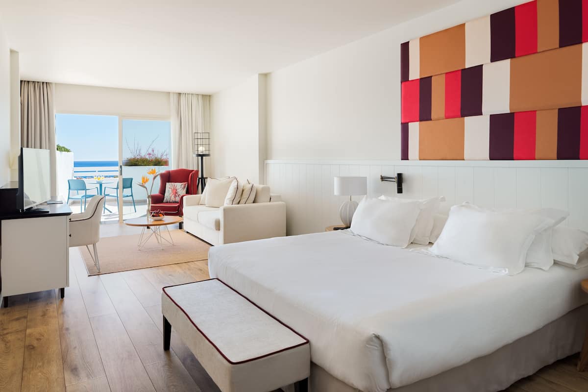 A hotel room with a large bed, a desk, a chair, and a view of the ocean.