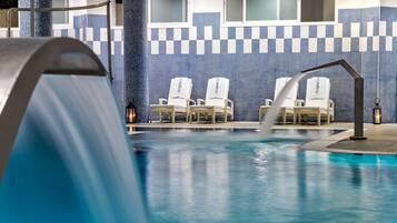 A swimming pool with a water feature, lounge chairs, and a tiled wall with a checkered pattern.
