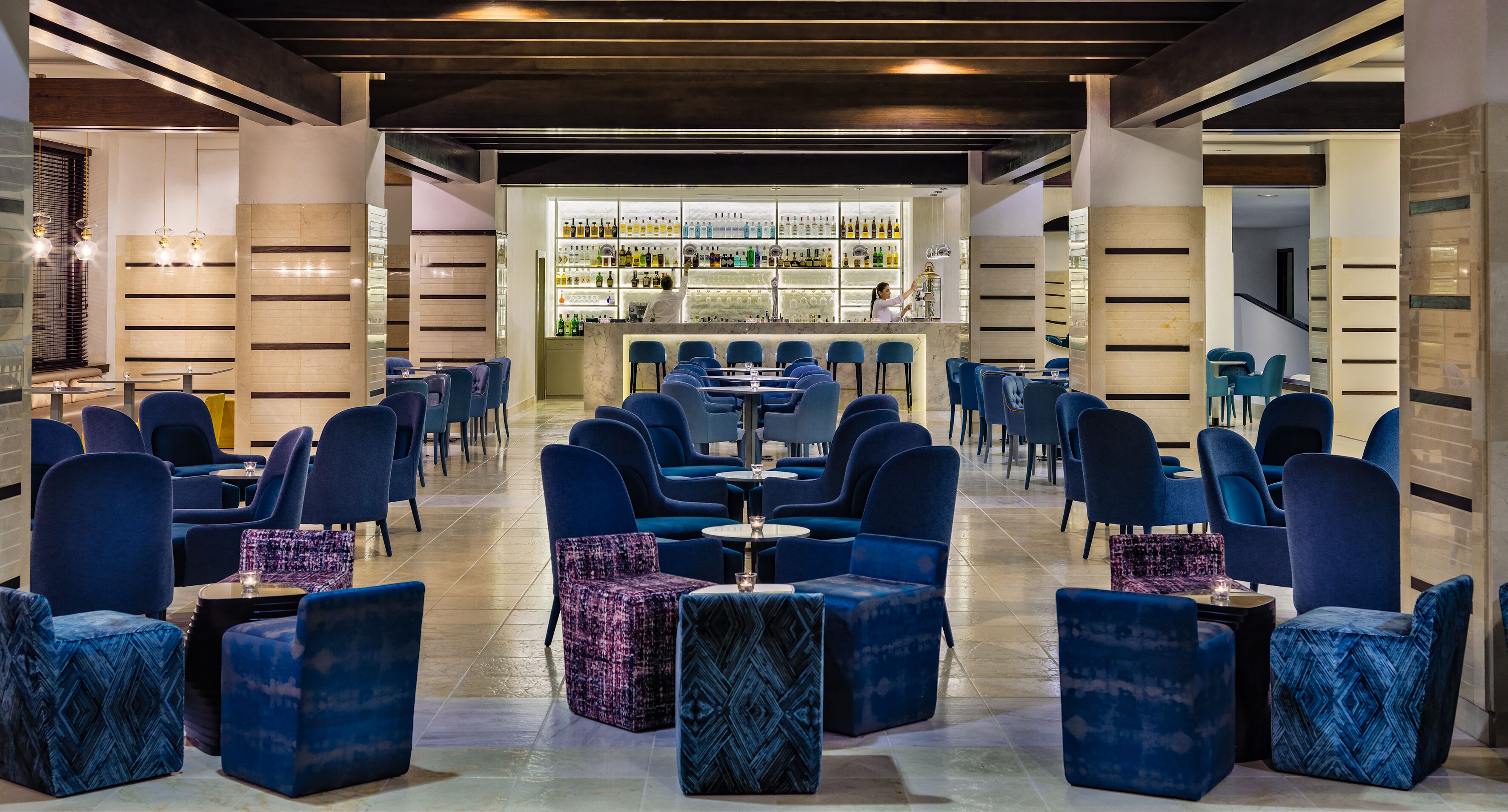 A modern bar area with a long counter, blue seating, and a well-stocked bar.