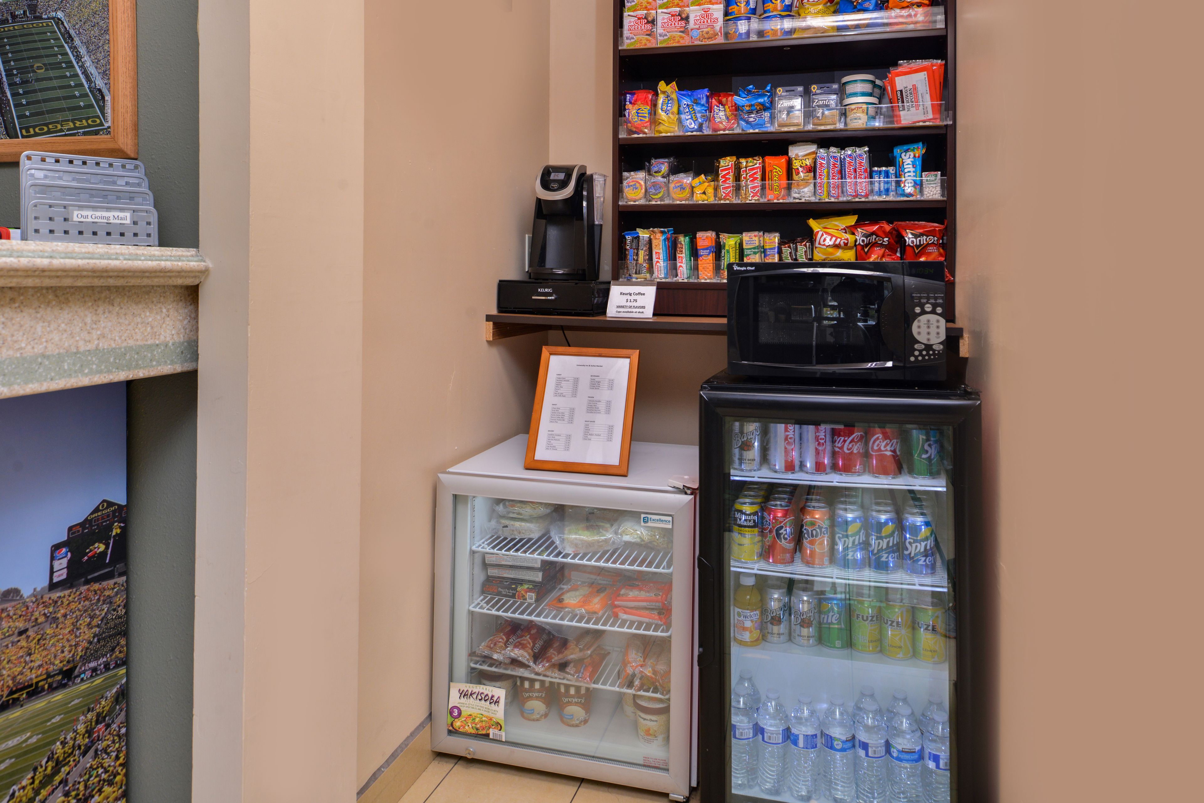 Una pequeña tienda de conveniencia con una máquina de café, estantes de snacks, una sección refrigerada y un enfriador de bebidas.