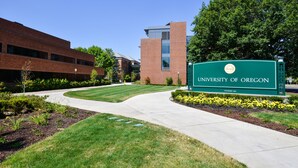 A University of Oregon campus sign with a brick building in the background.