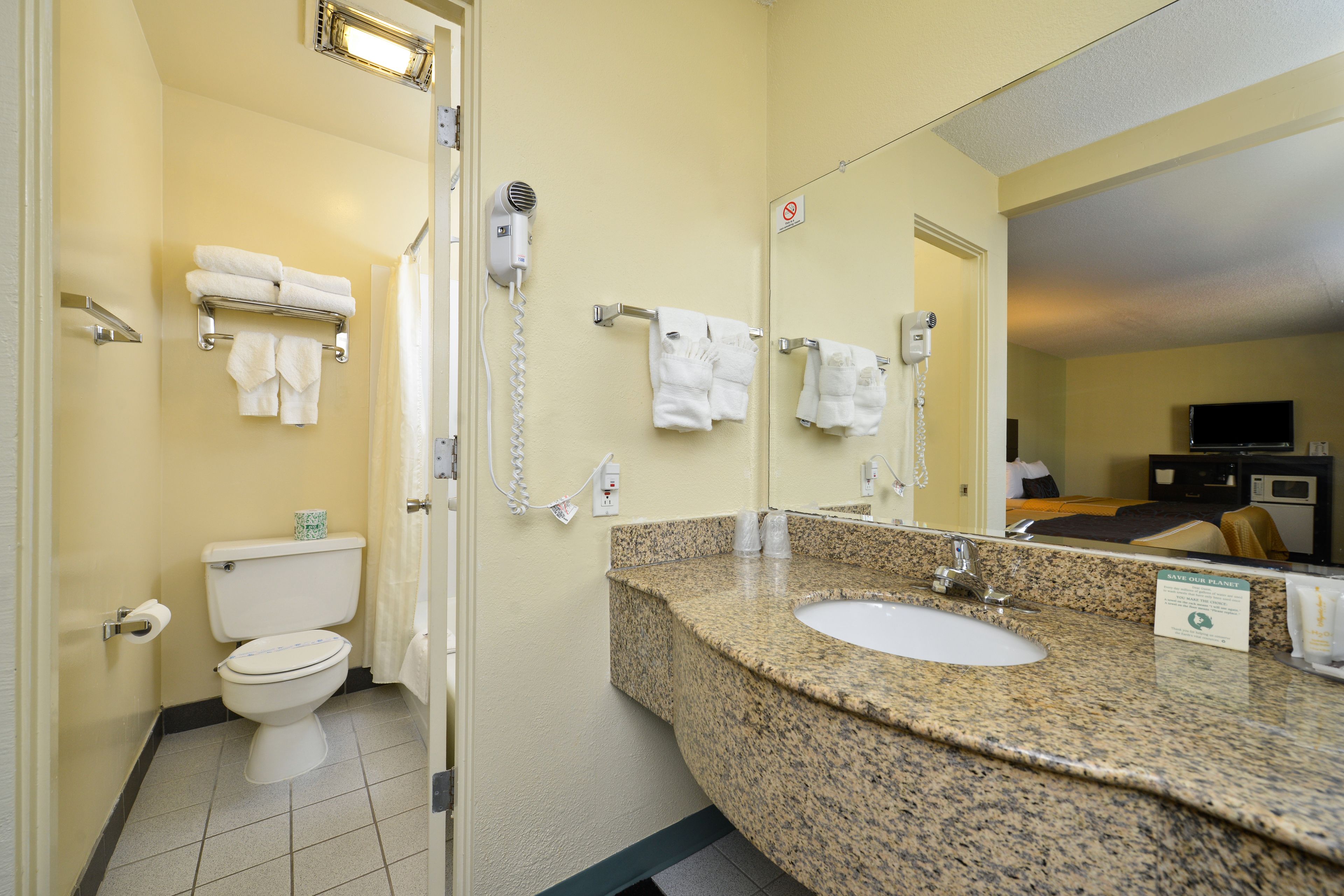 A hotel bathroom with a toilet, sink, and shower. There are towels hanging on the wall and a hairdryer on the wall.