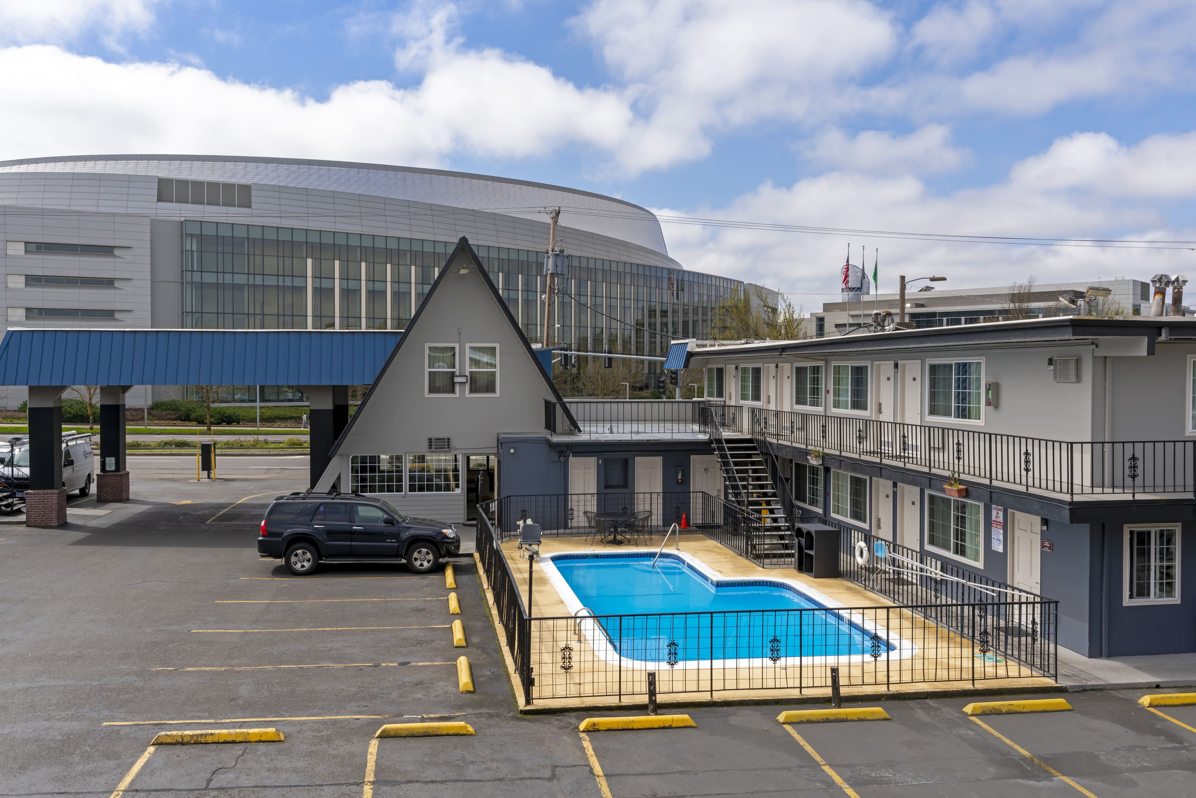 A hotel with a swimming pool, a covered parking area, and a modern building in the background.