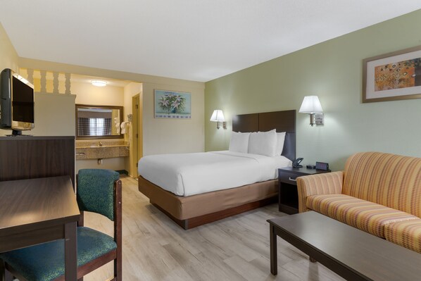 A hotel room with a bed, a desk, a chair, a sofa, and a TV. - University Inn & Suites (Eugene)