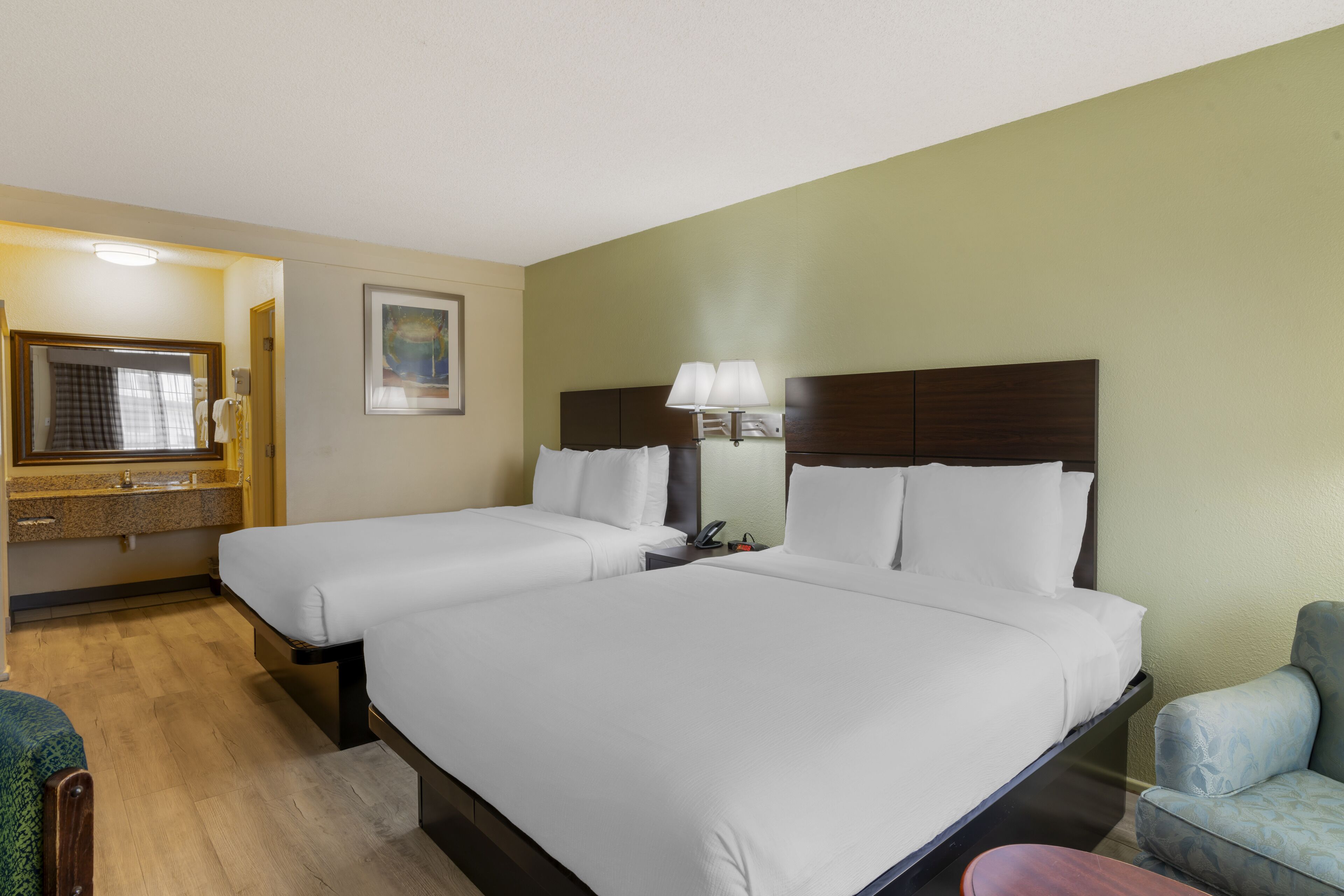 Habitación de hotel con dos camas, baño con espejo y una silla.