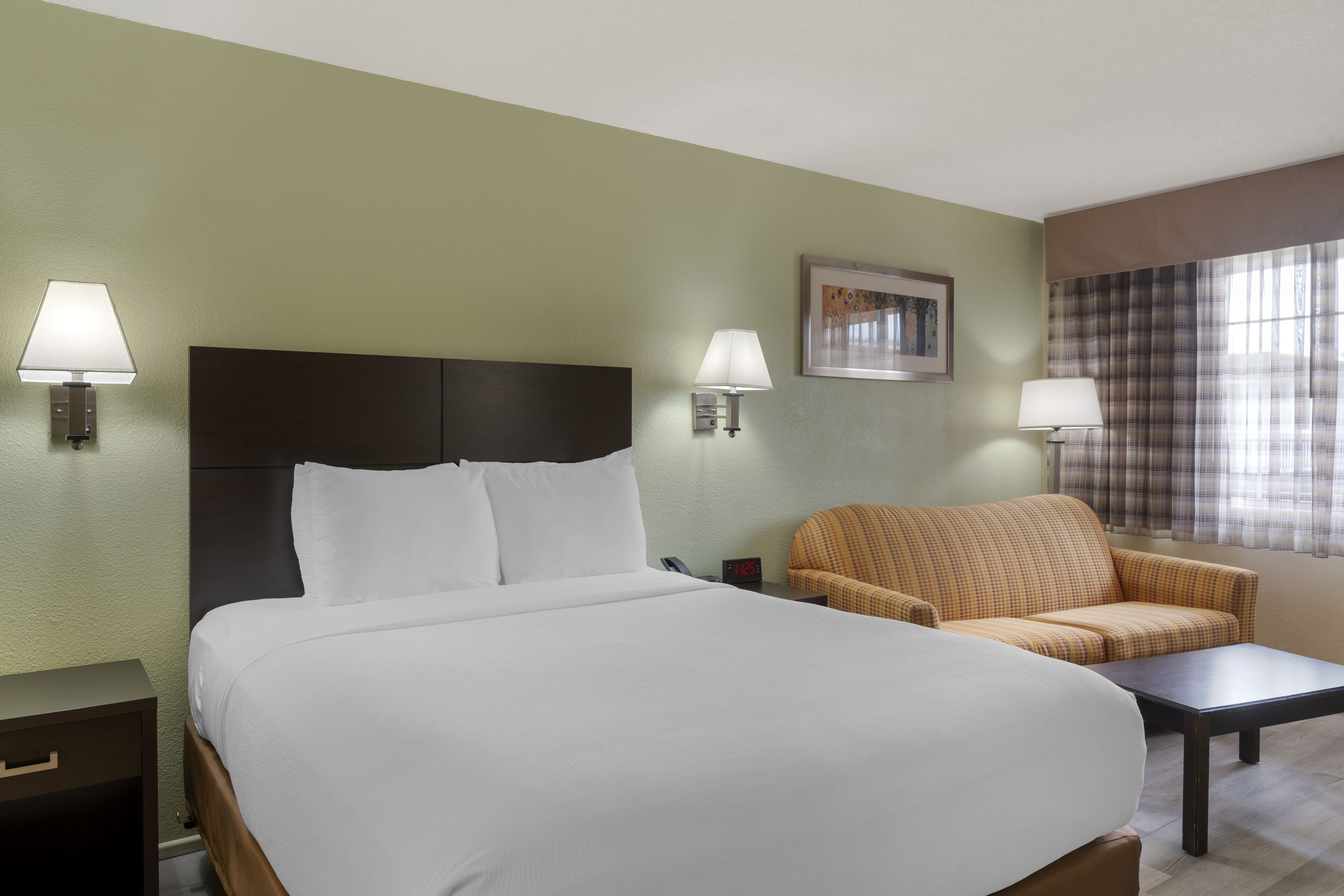 Ein Hotelzimmer mit einem großen Bett, zwei Wandlampen, einem Sofa, einem kleinen Tisch und einem Fenster mit Vorhängen.