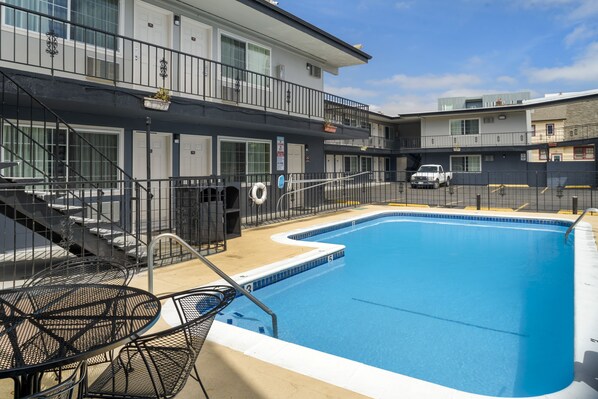 A swimming pool with a clear blue water, surrounded by a metal fence. There are steps leading to a balcony with a black railing.