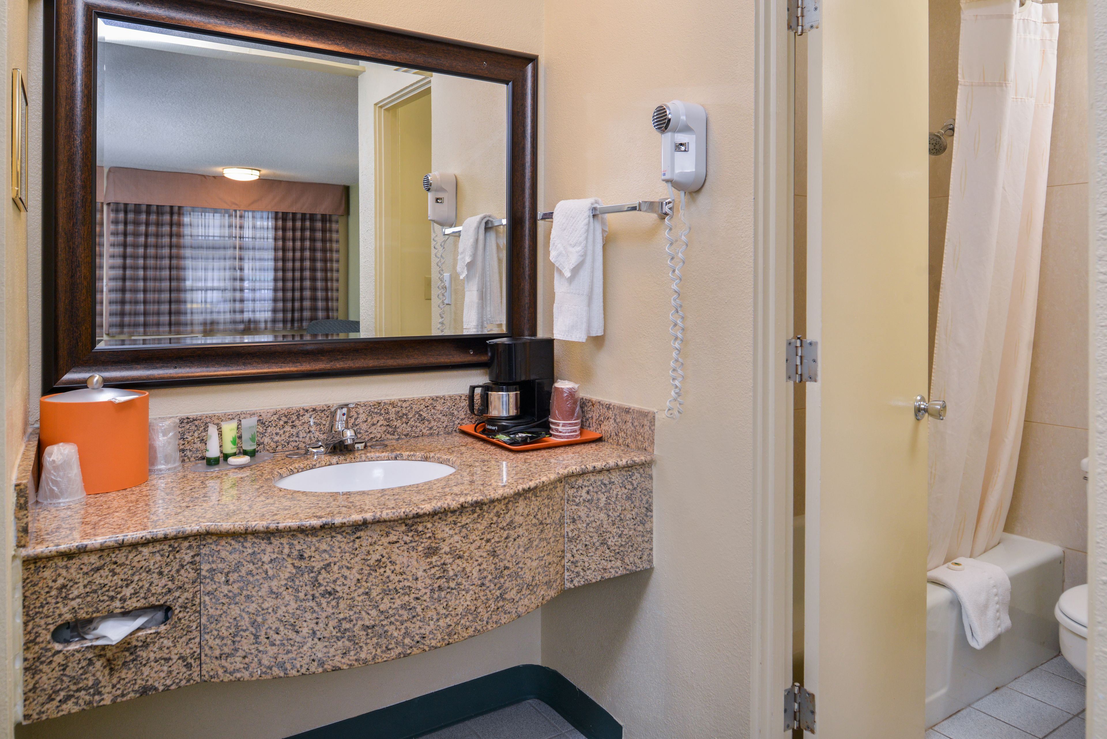 Une salle de bain avec un comptoir en granit, un lavabo, un miroir, un sèche-cheveux et un rideau de douche.