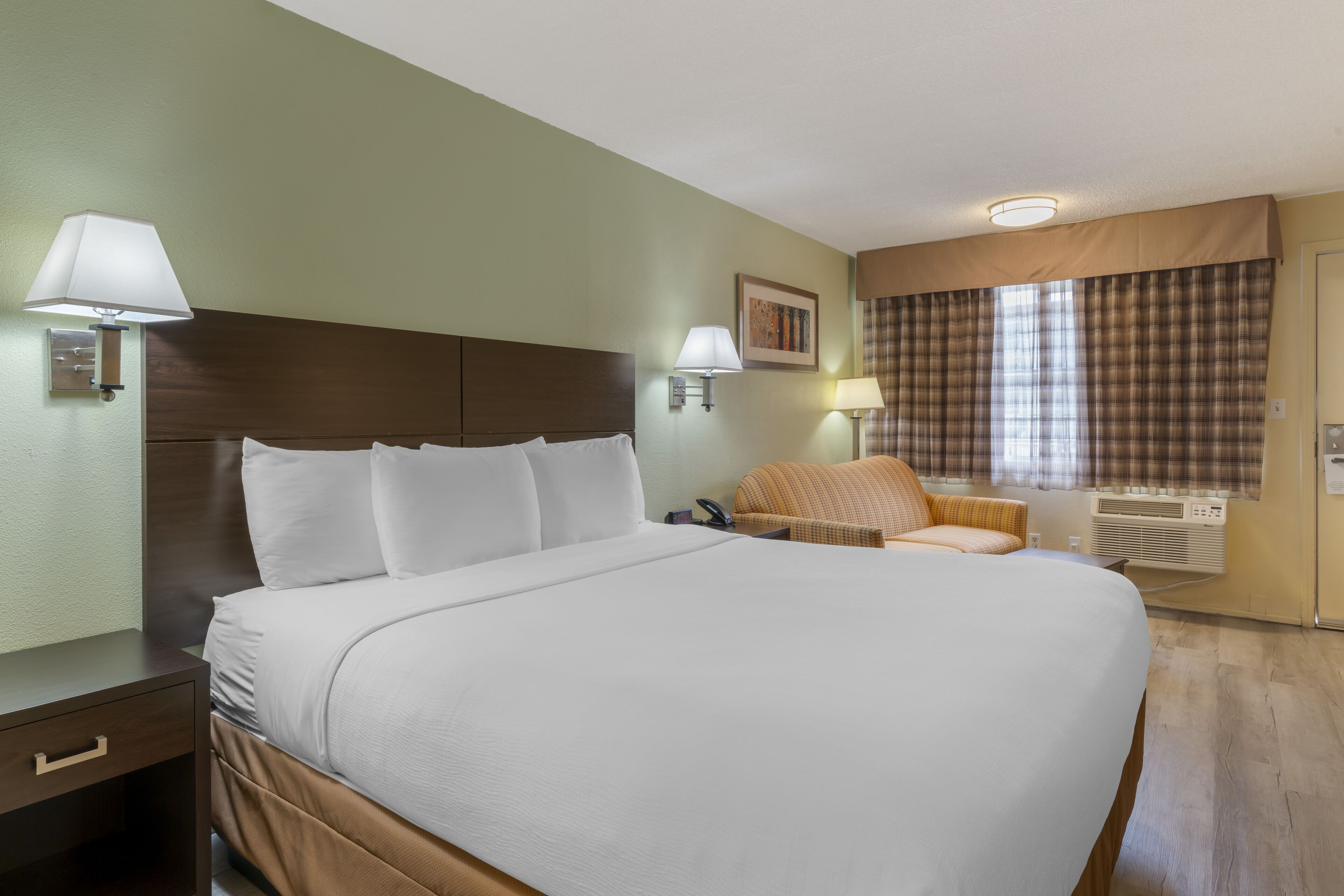 Une chambre d’hôtel avec un grand lit, des tables de chevet, une chaise et une fenêtre avec des rideaux.