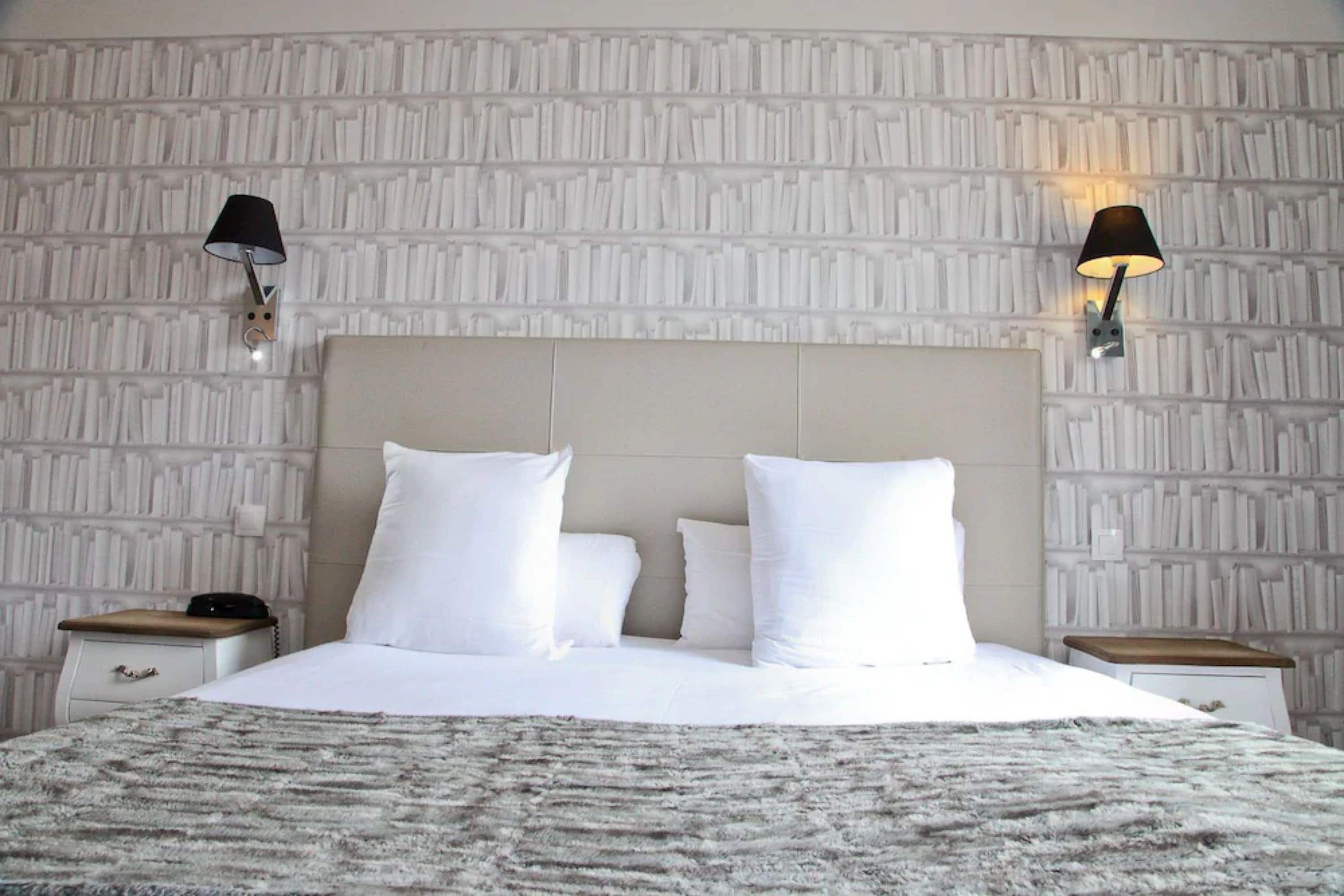 A neatly made bed with white linens and a fluffy gray blanket, two bedside tables with lamps, and a textured wall behind the bed.