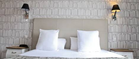 A neatly made bed with white linens and a fluffy gray blanket, two bedside tables with lamps, and a textured wall behind the bed.